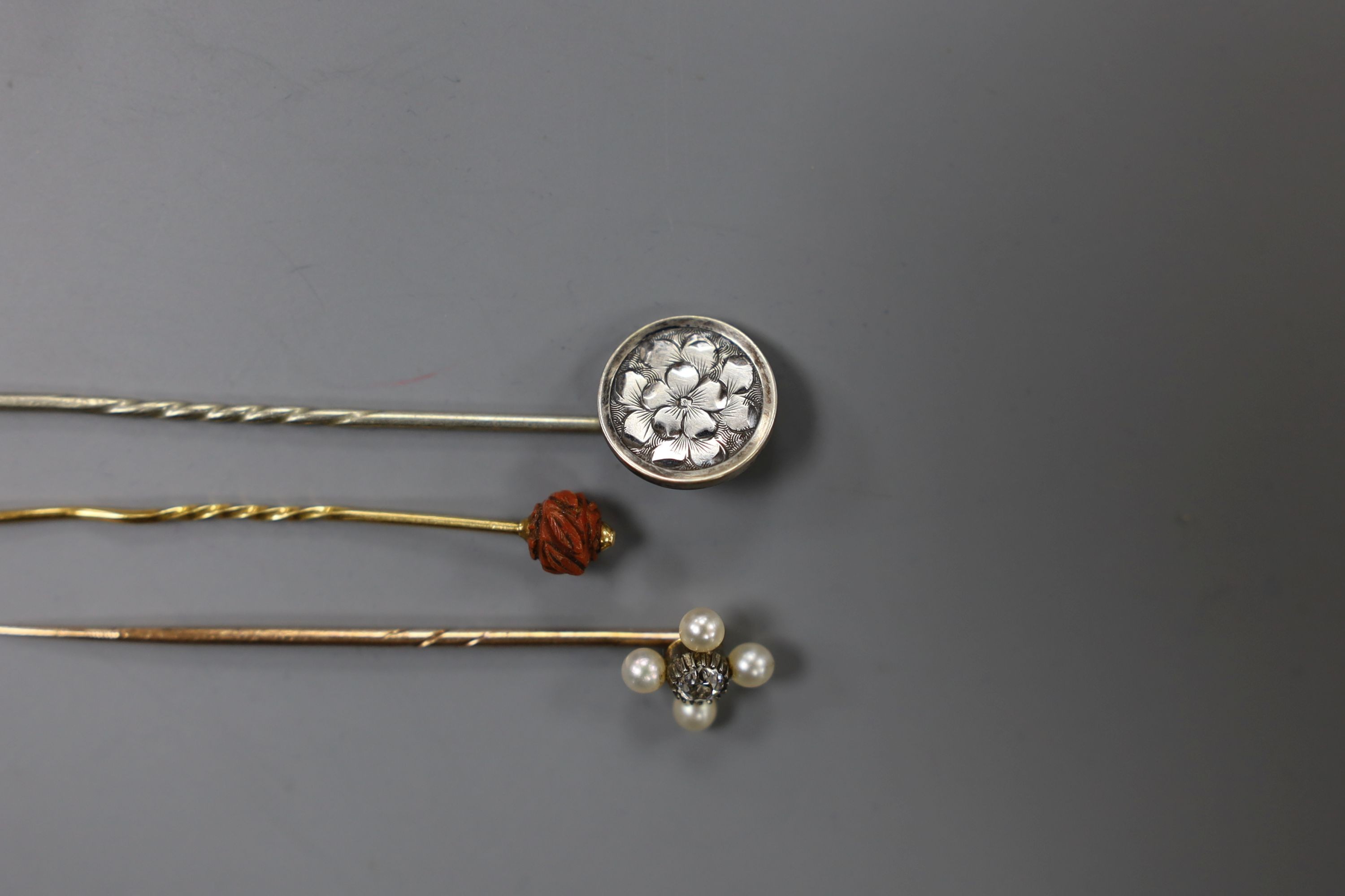 An Edwardian yellow metal, seed pearl and diamond set stick pin, 57mm and two other stick pins.